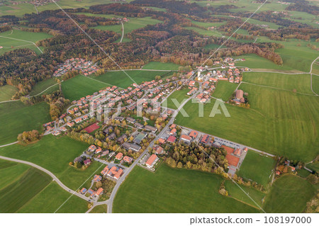 Aerial view of small town with red tiled roofs among green farm fields and distant forest in summer. 108197000