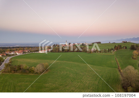 Aerial view of small scattered farm houses with red tiled roofs among green farming fields and distant mountain forest in summer. 108197004