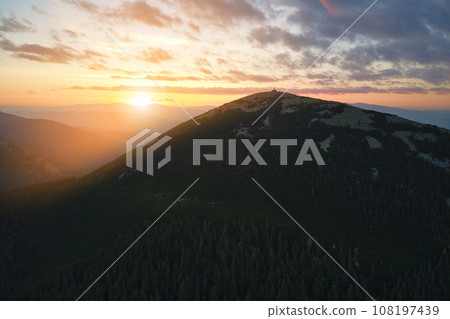 Aerial view of bright foggy morning over dark peak with mountain forest trees at autumn sunrise. Beautiful scenery of wild woodland at dawn Aerial view of bright foggy morning over dark peak with mountain forest trees at autumn sunrise. Beautiful scenery of wild woodland at dawn 108197439