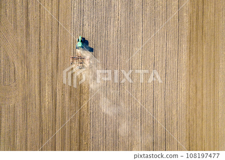 Aerial view of a tractor plowing black agriculture farm field after harvesting in autumn. Aerial view of a tractor plowing black agriculture farm field after harvesting in autumn. 108197477