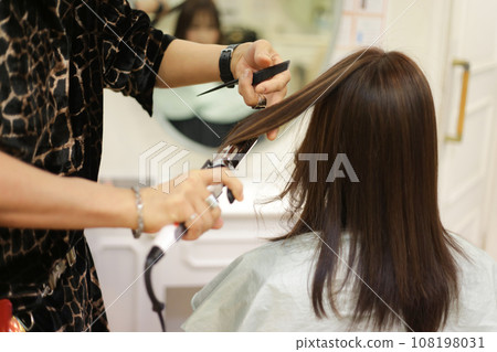 Male hairdresser ironing a woman's hair Male hairdresser ironing a woman's hair 108198031