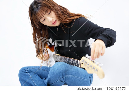 Image of a woman tuning an electric guitar Image of a woman tuning an electric guitar 108199372