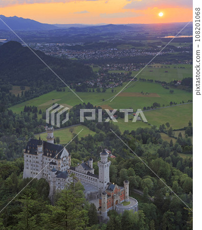 Aerial view of Neuschwanstein Castle at sunset with orange sky and sun the background Aerial view of Neuschwanstein Castle at sunset with orange sky and sun the background 108201068