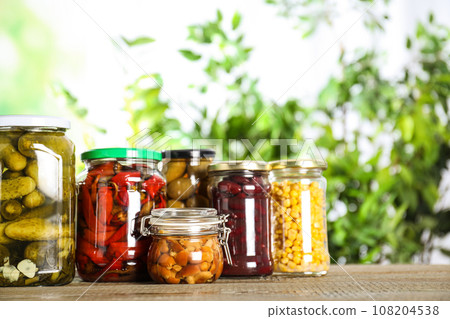 Glass jars of different pickled vegetables on wooden table 108204538
