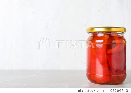 Glass jar of pickled red bell peppers on light marble table. Space for text Glass jar of pickled red bell peppers on light marble table. Space for text 108204540