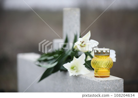 White lilies and candle on light grey granite tombstone outdoors. Funeral ceremony White lilies and candle on light grey granite tombstone outdoors. Funeral ceremony 108204634