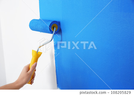 Woman painting white wall with blue dye, closeup. Interior renovation Woman painting white wall with blue dye, closeup. Interior renovation 108205829