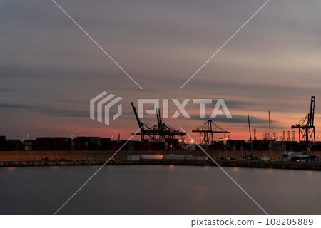 Dusk at the bustling commercial port with silhouette of giant cranes Dusk at the bustling commercial port with silhouette of giant cranes 108205889