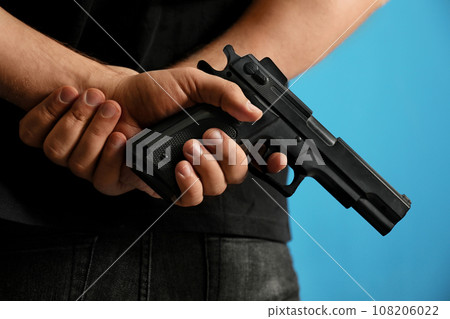Man holding gun on blue background, closeup Man holding gun on blue background, closeup 108206022