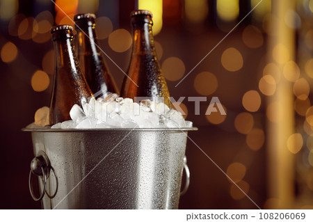 Beer in metal bucket with ice against blurred lights, closeup Beer in metal bucket with ice against blurred lights, closeup 108206069