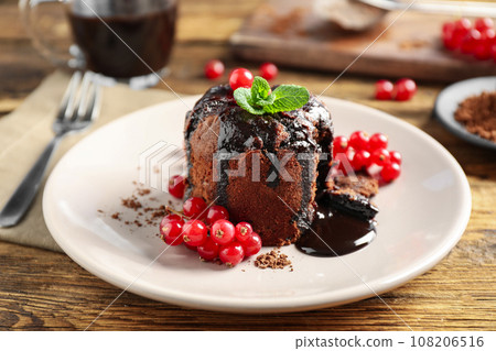 Delicious warm chocolate lava cake with mint and berries on wooden table, closeup Delicious warm chocolate lava cake with mint and berries on wooden table, closeup 108206516