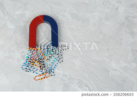 Magnet attracting paper clips on grey marble table, flat lay. Space for text Magnet attracting paper clips on grey marble table, flat lay. Space for text 108206683