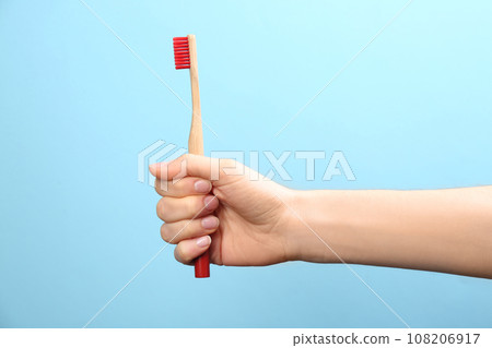 Woman holding bamboo toothbrush on light blue background, closeup 108206917