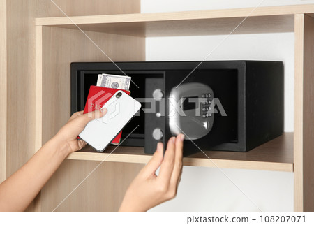 Woman putting smartphone, passport and money into steel safe, closeup 108207071