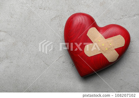 Red wooden heart with sticking plasters on light grey stone table, top view. Space for text 108207102