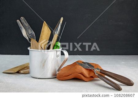 Tools for modeling from clay and plasticine on a light stone table against the background of a black wall in a sculptor workshop Tools for modeling from clay and plasticine on a light stone table against the background of a black wall in a sculptor workshop 108208607