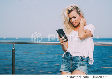 Charming female watching mobile in seafront Charming female watching mobile in seafront 108209068