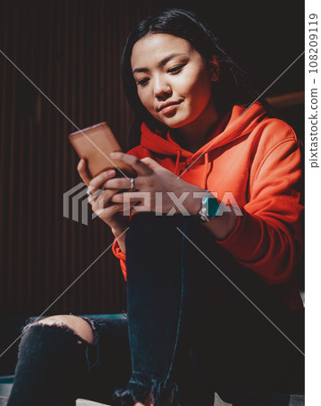 Chinese teenage woman installing new app for editing media files in offline mode on mobile phone Chinese teenage woman installing new app for editing media files in offline mode on mobile phone 108209119