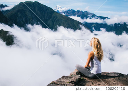Woman with blonde hair sitting in lotus pose on edge of rock Woman with blonde hair sitting in lotus pose on edge of rock 108209418