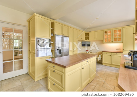 a kitchen with yellow cabinets and wood counter tops in the center of the room is an open door that leads out to a patio 108209450