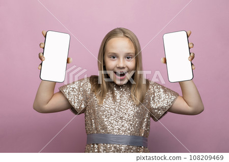 Happy surprised child with two phone. Little girl holding smartphone with blank empty white screen Happy surprised child with two phone. Little girl holding smartphone with blank empty white screen 108209469