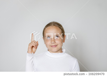 Cute child pointing finger up on white studio wall background Cute child pointing finger up on white studio wall background 108209470