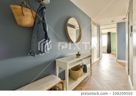 a hallway with a bench, mirror and coat rack hanging on the wall next to it is a basket filled with clothes 108209502