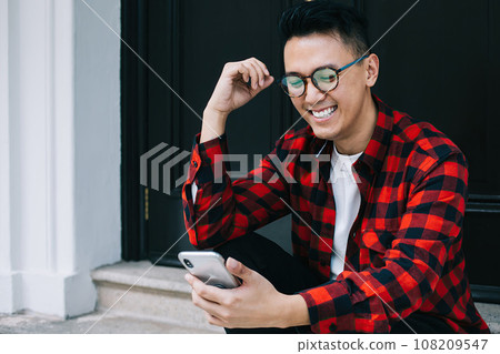 Happy young ethnic man enjoying pastime with smartphone on stairs 108209547