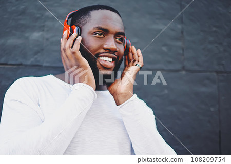 Carefree male meloman listening music with high volume using headphones at publicity area, 108209754