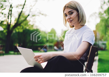 Student sitting on bench with laptop and looking at camera 108209757