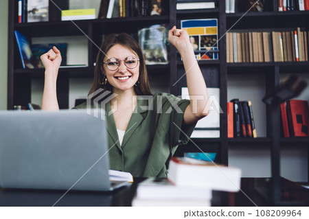Excited female student sitting with and raising fists Excited female student sitting with and raising fists 108209964