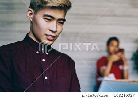 Serious Asian man browsing laptop in workspace Serious Asian man browsing laptop in workspace 108210027