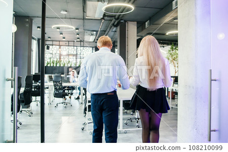 Stylish young man and woman at official style clothes which walking through the office room. 108210099