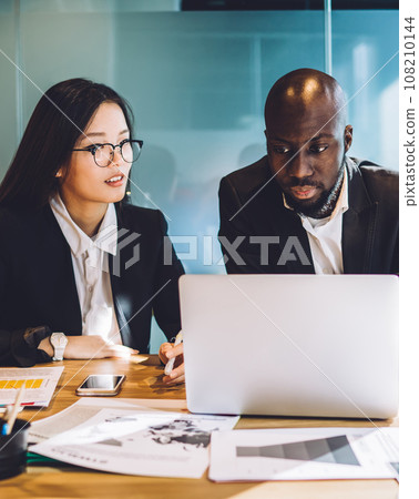 Multiethnic business partners working on project together with laptop at conference room Multiethnic business partners working on project together with laptop at conference room 108210144