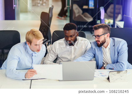 Businessmen sitting at the office table and comparing data from report and computer to succeed in corporate working together. Businessmen sitting at the office table and comparing data from report and computer to succeed in corporate working together. 108210245