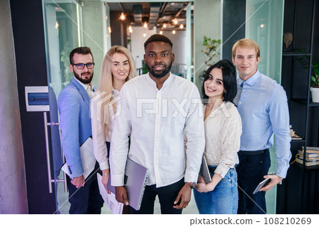 Successful young multiracial work team of handsome men and pretty women which looking at camera with sincerely smiles on the background of the modern stylish office. 108210269