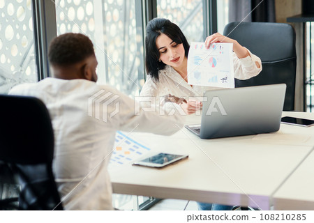 Likable purposeful business partners carefully studying financial documents with charts at the boardroom table at the meeting room. Likable purposeful business partners carefully studying financial documents with charts at the boardroom table at the meeting room. 108210285