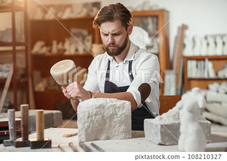 Stone carver works with wooden hammer and chisel at limestone. 108210327