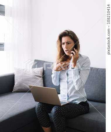 Amazed woman calling on phone sitting with computer Amazed woman calling on phone sitting with computer 108210414