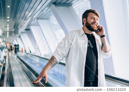 Enthusiastic man talking on smartphone riding on modern travelator in light tunnel 108211020
