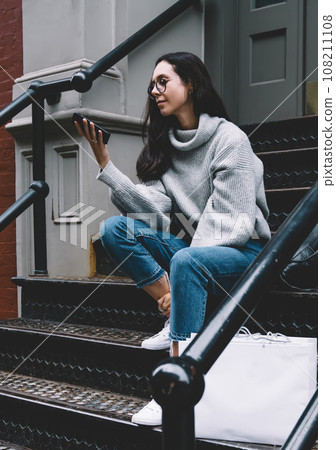 Young woman sitting on stair surfing mobile on street 108211108
