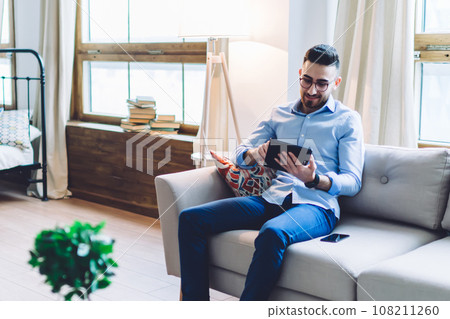 Modern guy and lady using electronic devices sitting across each other in light apartment Modern guy and lady using electronic devices sitting across each other in light apartment 108211260