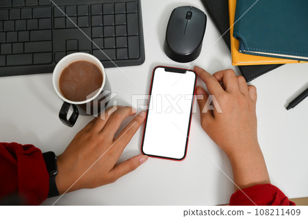 Overhead view of woman using mobile phone on white office desk. Empty screen for advertising text message 108211409