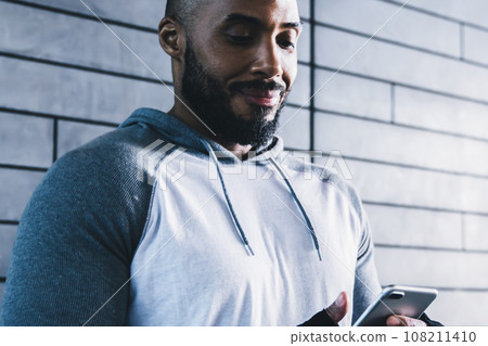 Athletic sporty black male browsing mobile in gym Athletic sporty black male browsing mobile in gym 108211410