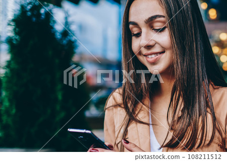 Positive pretty brunette girl sending text message via smartphone chatting online with friend Positive pretty brunette girl sending text message via smartphone chatting online with friend 108211512