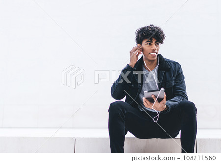 Young ethnic man with tablet listening to music and looking away 108211560