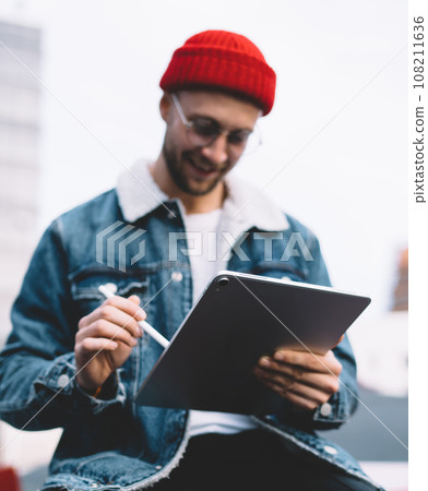 Glad trendy male sitting on cube and using tablet Glad trendy male sitting on cube and using tablet 108211636