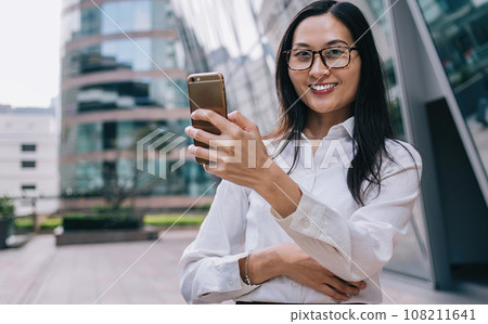 Joyful female browsing smartphone on street Joyful female browsing smartphone on street 108211641