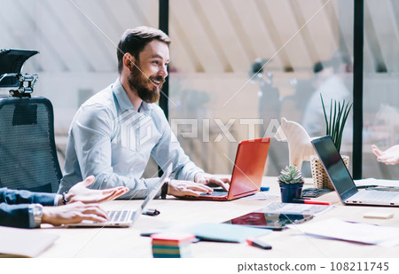Cheerful colleagues interacting in office with laptops 108211745