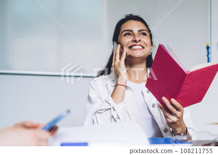 Laughing casual woman speaking on phone in classroom Laughing casual woman speaking on phone in classroom 108211755